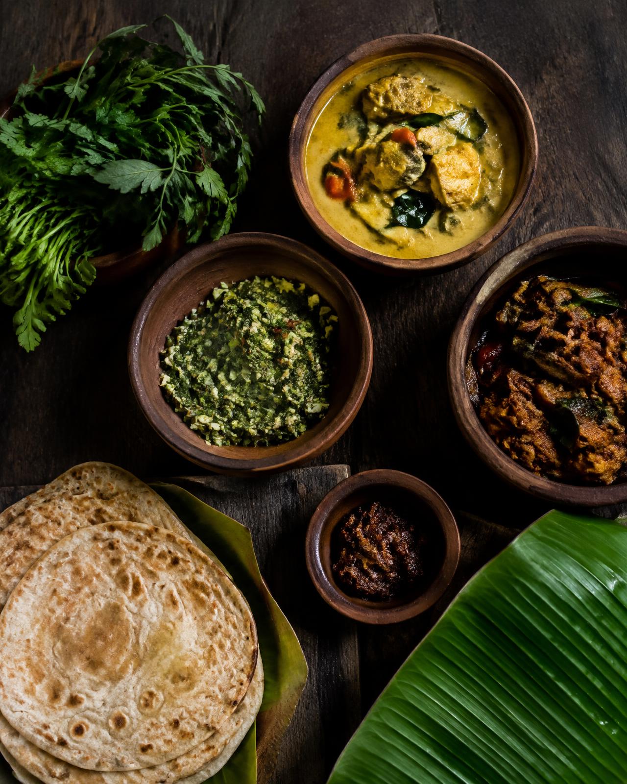 Clay bowls of local curries, herbs and flatbread on a dark wooden table