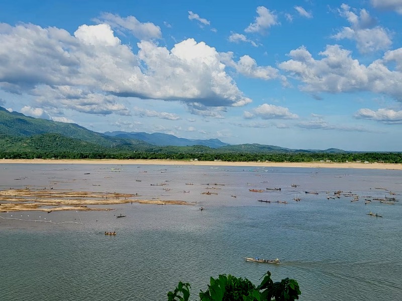 Fishing boats on a wide river below forested hills