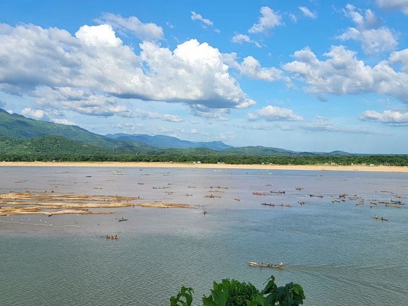 A wide river dotted with small fishing boats below the green hills